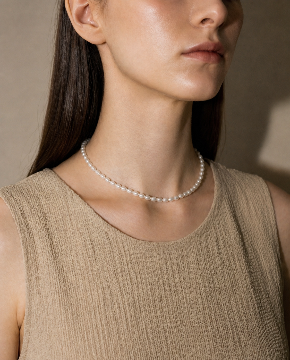 女性がOUIのPerle Necklace N011を着用した首元のスタイリング写真です。ベージュのタンクトップを着て、首元のパールネックレスがきわ際立っています。